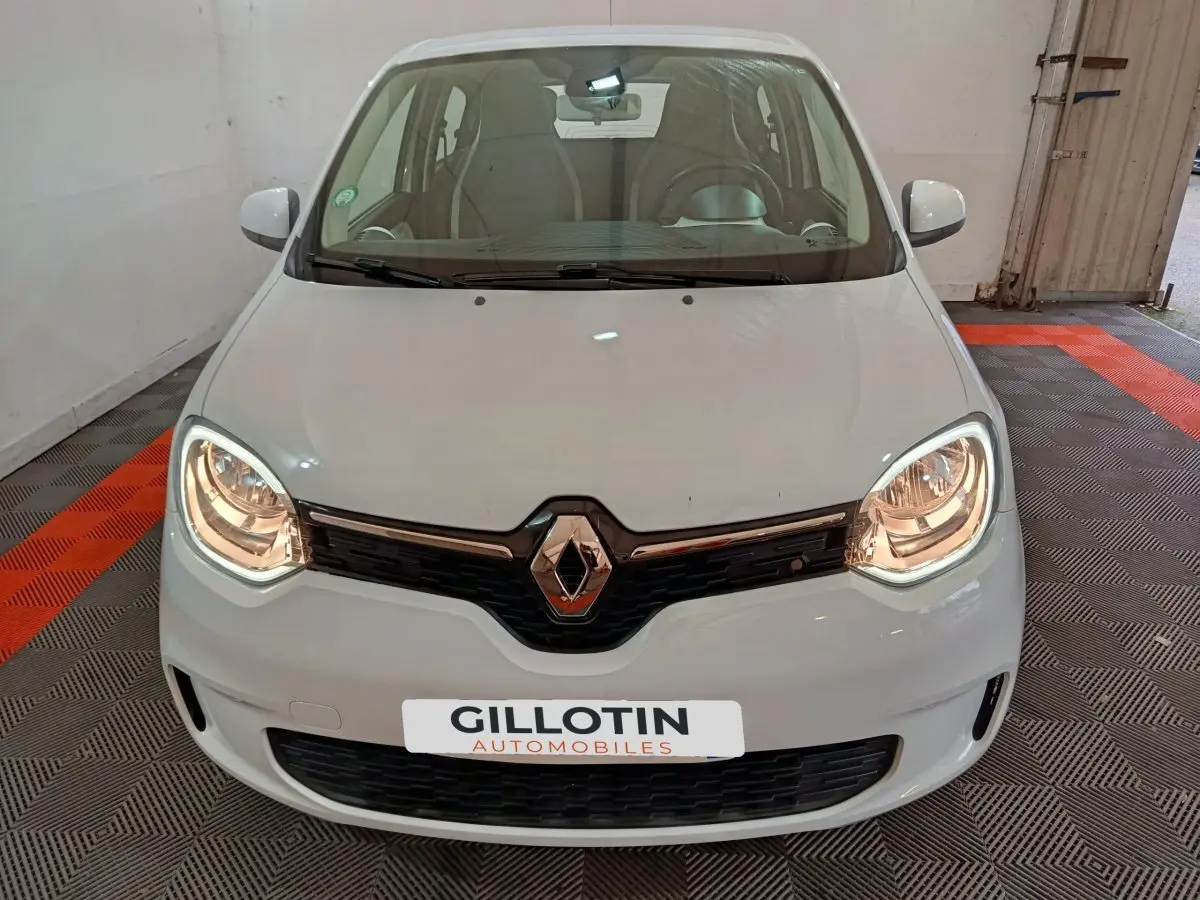 Vue frontale d'une Renault Twingo Zen blanche de 2021 avec phares allumés et logo Renault bien visible.
