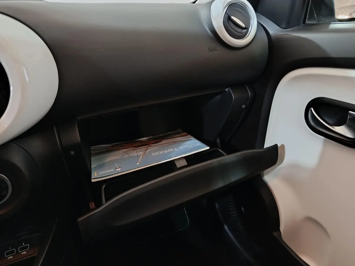 Vue intérieure côté passager de la Renault Twingo Zen blanche 2021 avec boîte à gants ouverte et manuel visible.