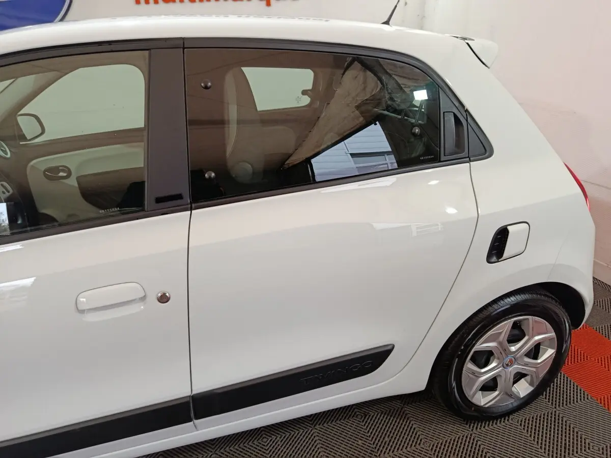 Vue latérale droite d'une Renault Twingo Zen blanche avec poignées de porte intégrées et logo Twingo sur bas de caisse noir.