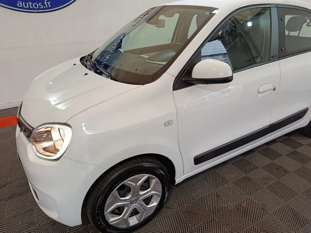 Renault Twingo Zen électrique blanche vue 3/4 avant droit, avec jantes spécifiques et rétroviseur blanc.
