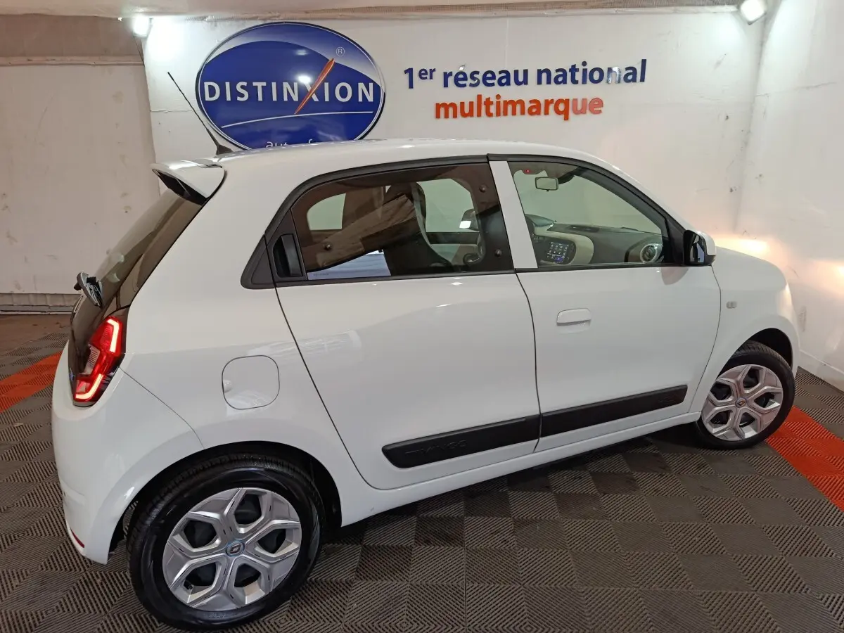 Vue côté droit de la Renault Twingo Zen électrique blanche de 2021, avec feux arrière LED allumés en intérieur showroom.