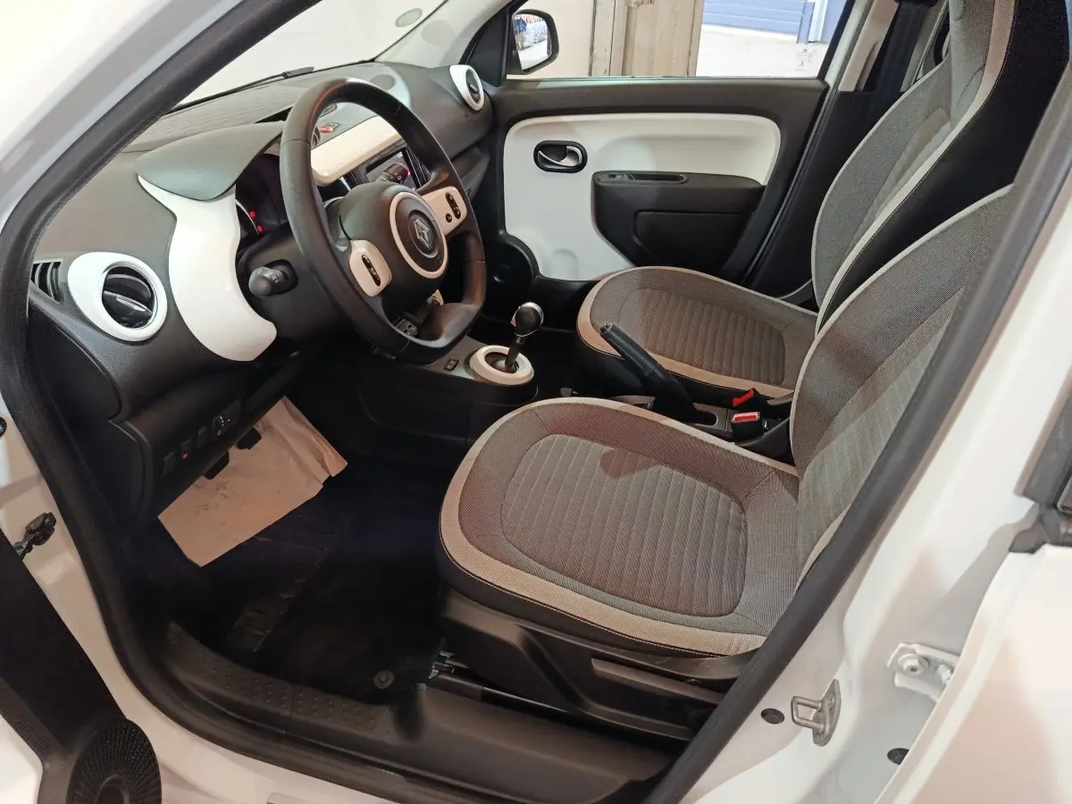 Vue intérieure côté conducteur de la Renault Twingo Zen blanche, avec tableau de bord et sièges gris en tissu.