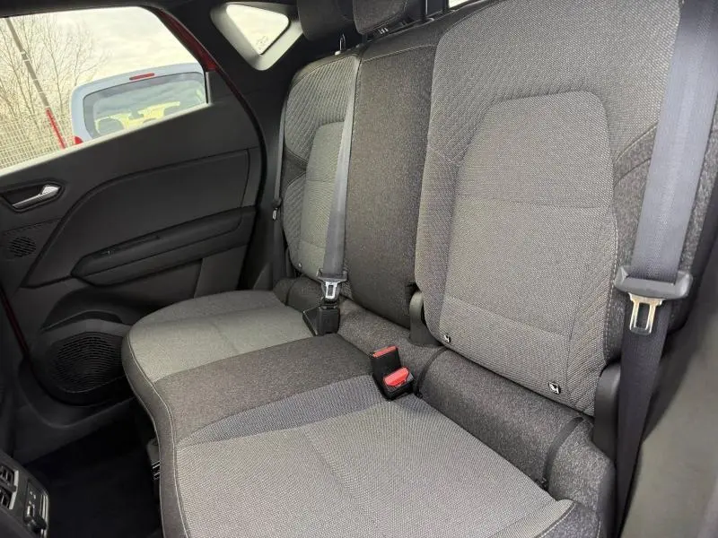 Vue intérieure des sièges arrière gris du Renault Captur 2025, avec ceinture de sécurité et porte côté gauche rouge visible.