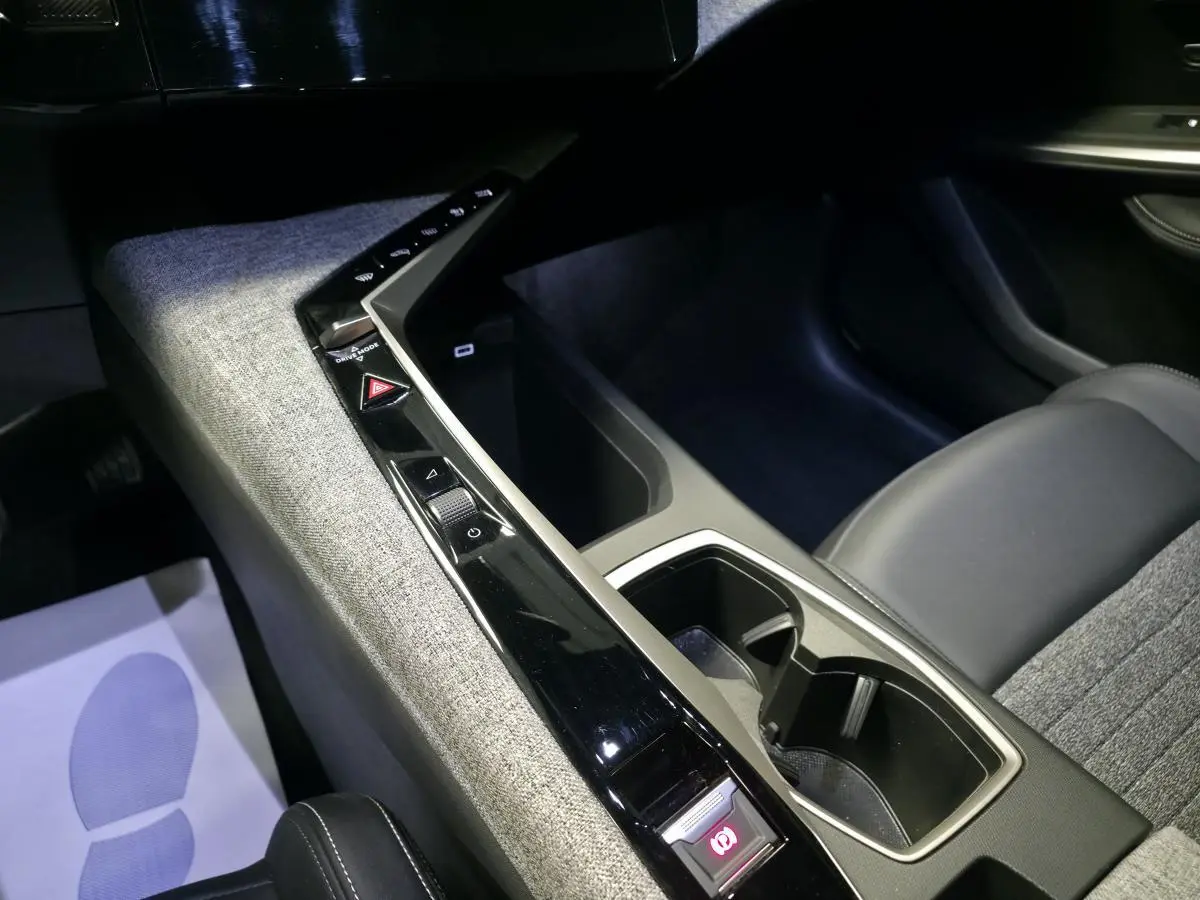 Vue intérieure rapprochée de la console centrale tissu gris et noir laqué du Peugeot 3008 Hybrid 2025.