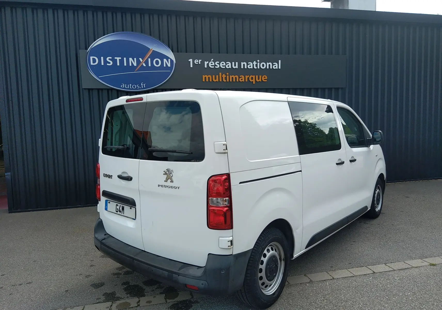 Vue 3/4 arrière droite d'un Peugeot Expert Fourgon blanc uni stationné devant un bâtiment gris.