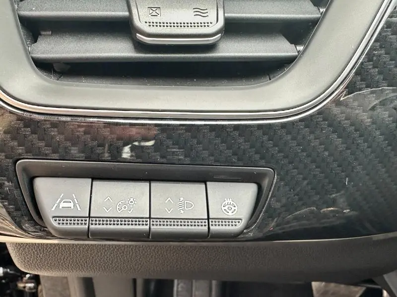 Gros plan sur les commandes d'assistance et réglages d'éclairage sur tableau de bord noir carbone d'une Renault Arkana.