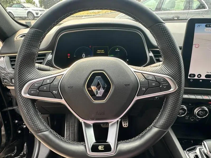 Vue rapprochée du volant noir perforé du Renault Arkana 2023 avec commandes multifonctions et tableau de bord numérique.