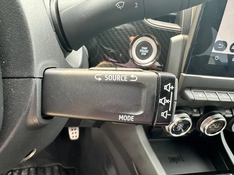 Gros plan sur la commande audio au volant noir du Renault Arkana 2023, avec bouton Start Engine Stop en arrière-plan.