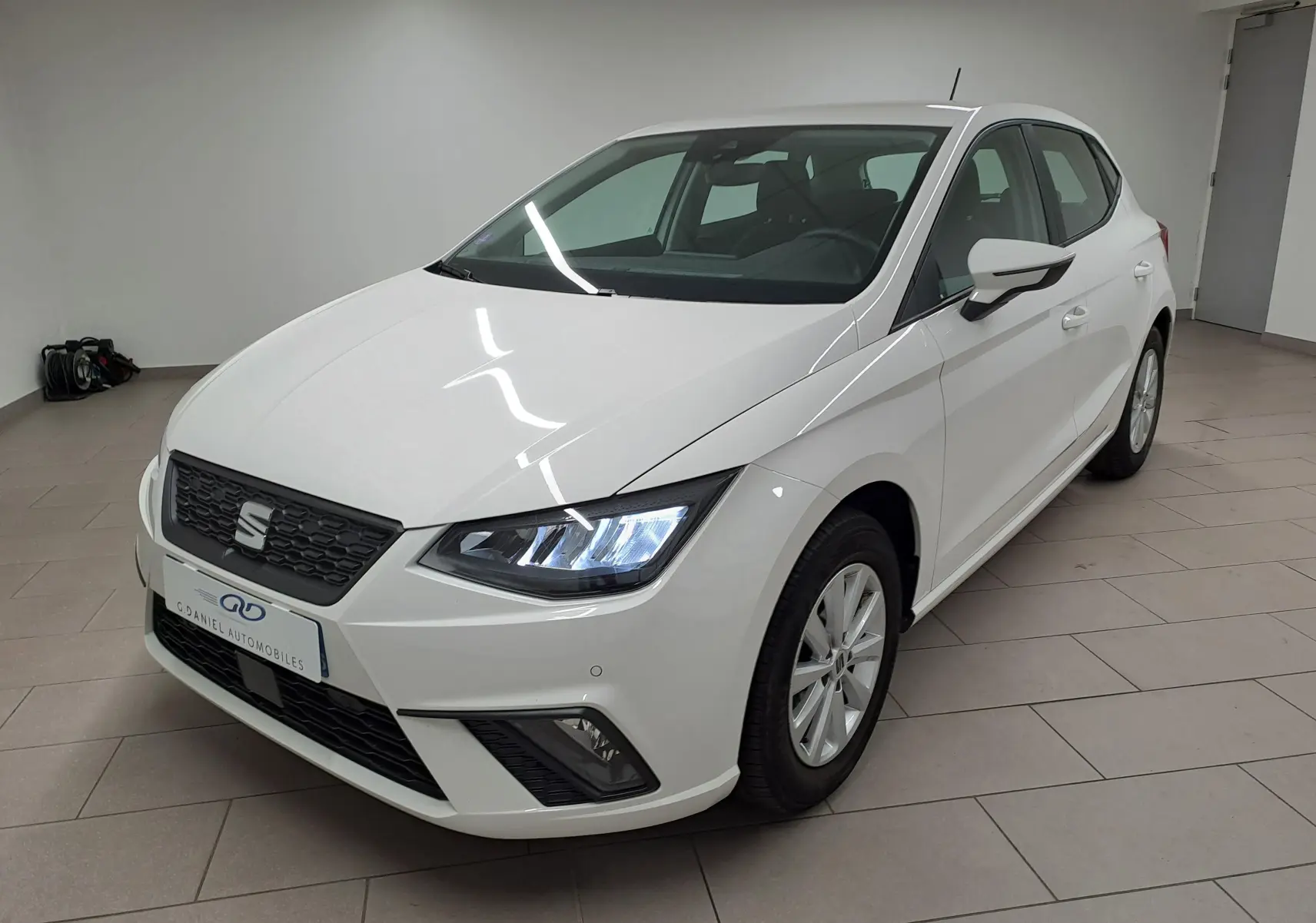 SEAT Ibiza 2023 blanc candy vue 3/4 avant droit avec phares allumés dans un showroom intérieur.