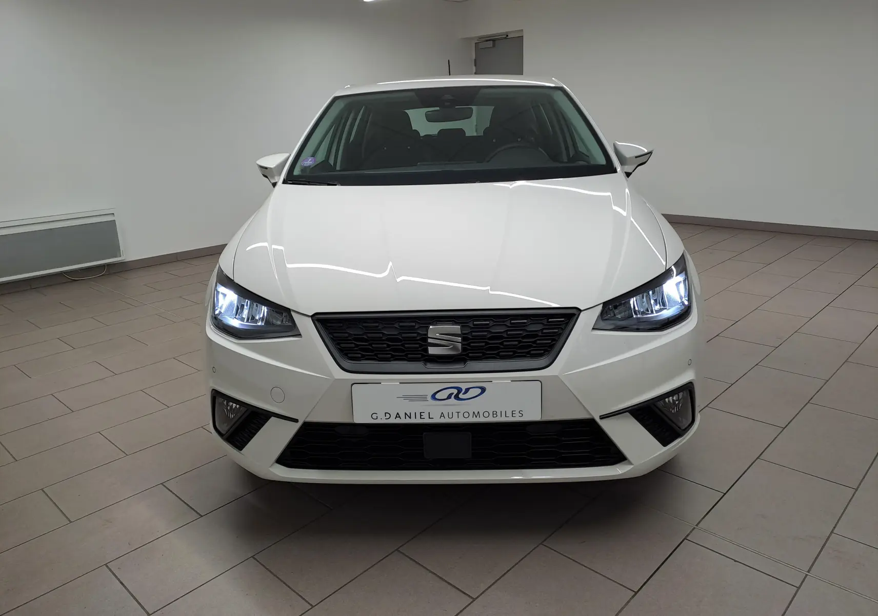 Vue frontale d'une SEAT IBIZA blanc candy 2023 avec phares allumés dans un showroom intérieur.