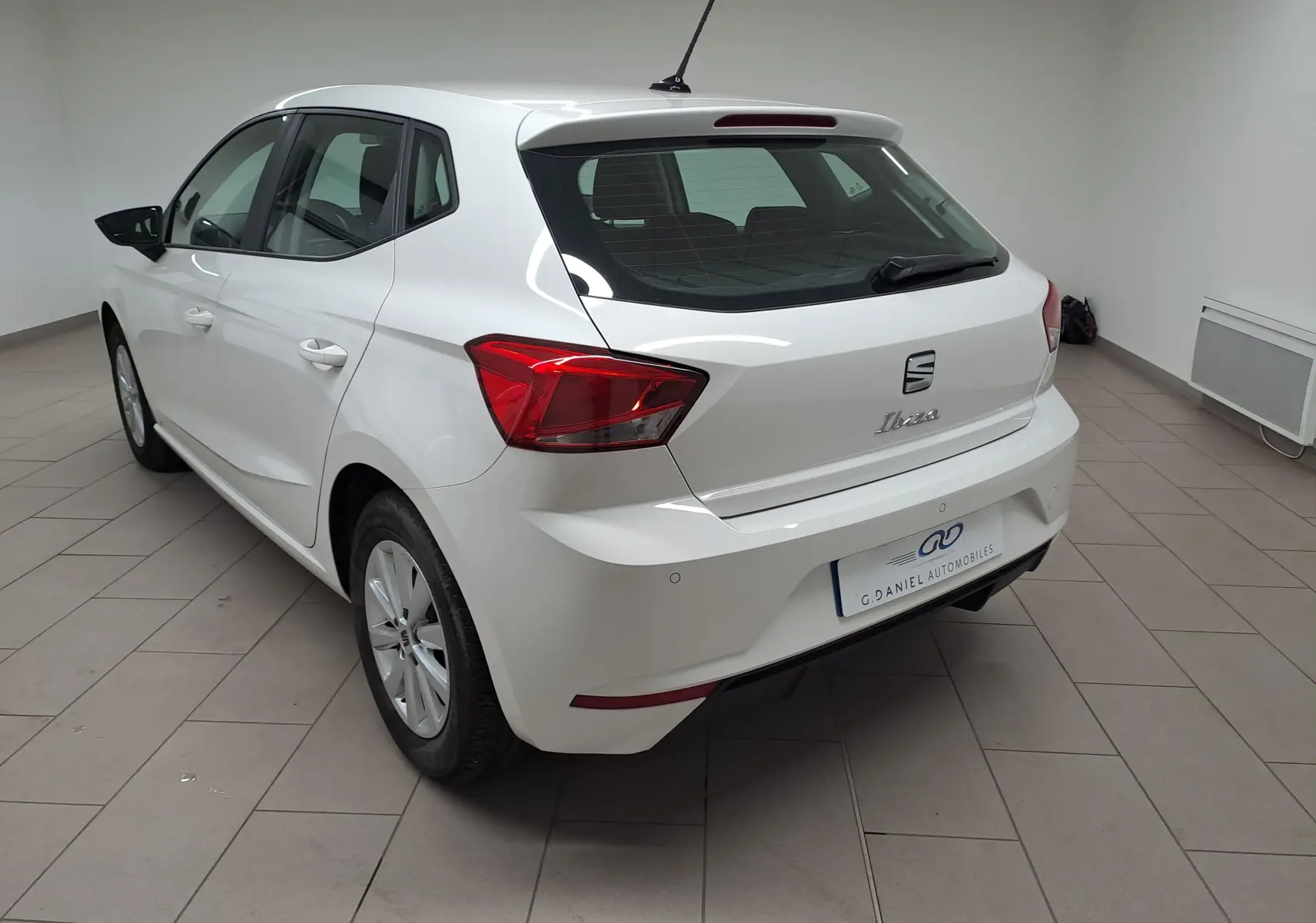 Vue 3/4 arrière droite d'une SEAT Ibiza blanche Candy 2023, finition Style Business, en intérieur showroom.