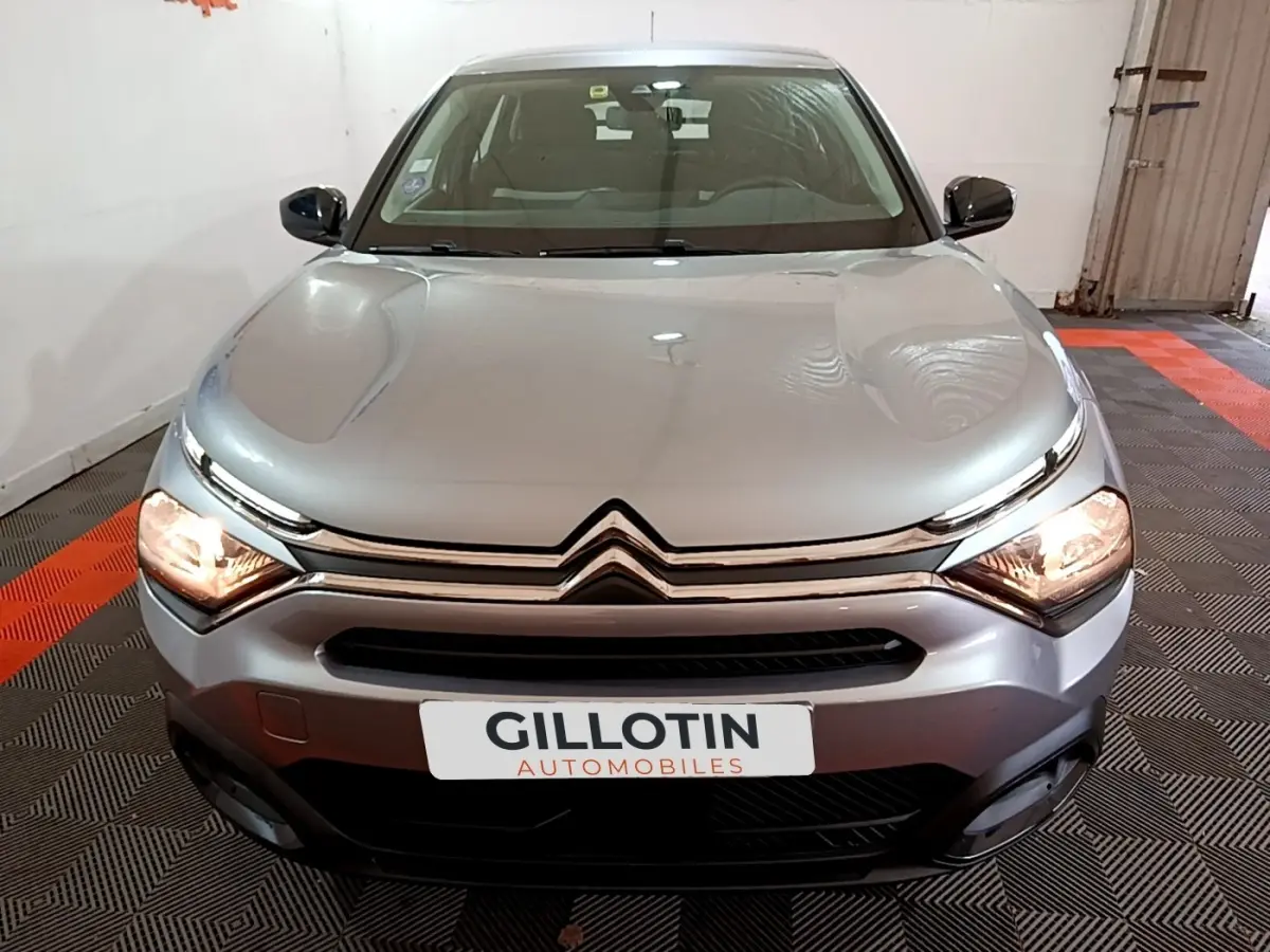 Vue avant d'une Citroën C4 gris foncé avec phares allumés dans un garage au sol damier noir et rouge.