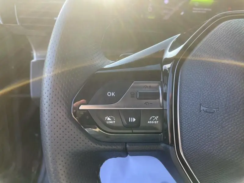 Gros plan sur les commandes au volant côté gauche du Peugeot 408 Hybrid 2024 noir métal, avec boutons d'assistance et limitation.