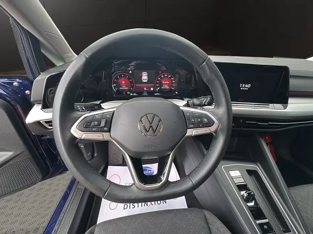 Vue centrée sur le volant multifonction noir de la Volkswagen Golf VIII bleu, avec tableau de bord digital et écran tactile.