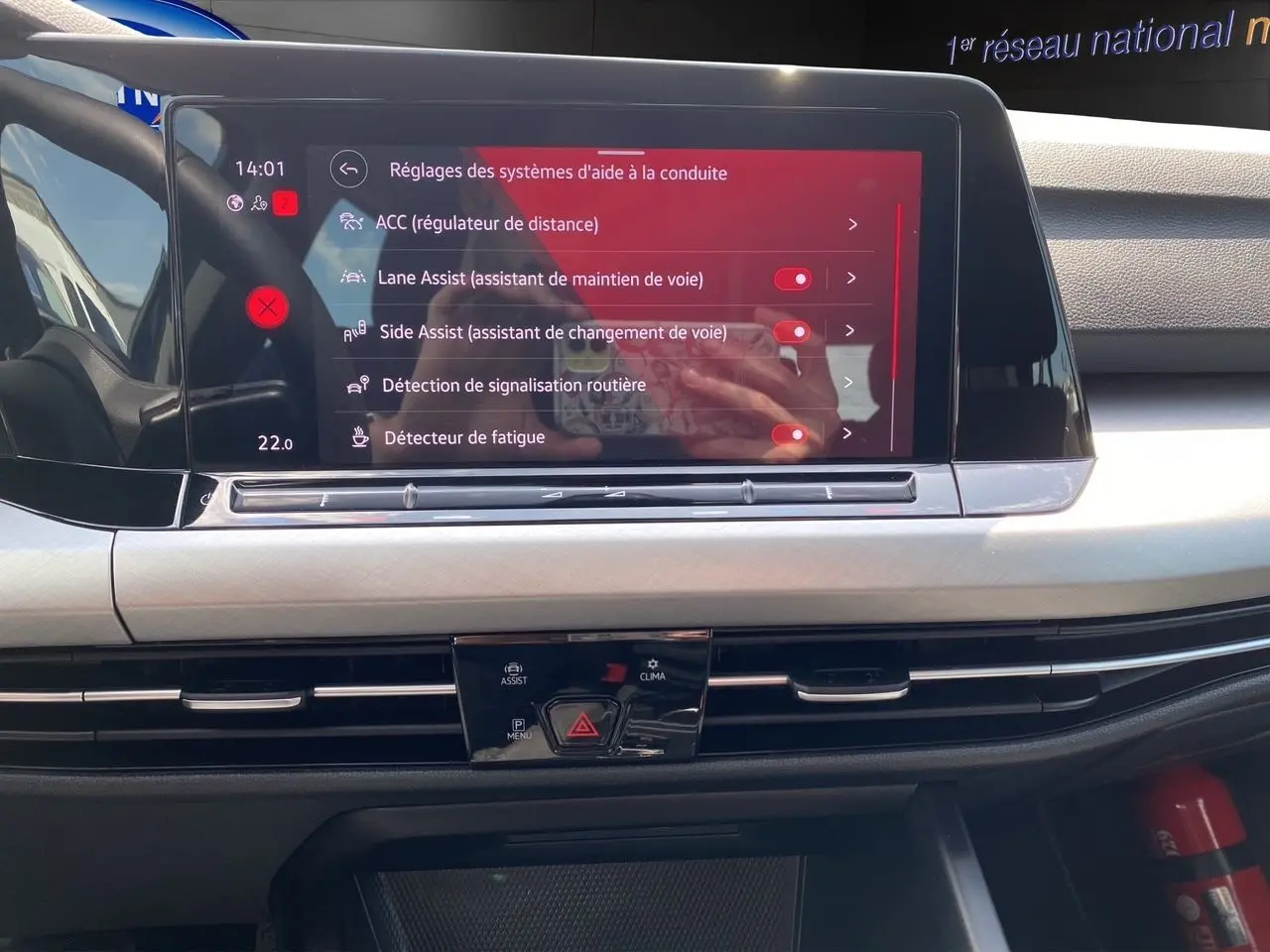 Écran tactile central de la Volkswagen Golf VIII 2023 affichant les réglages d'aides à la conduite dans un intérieur noir.