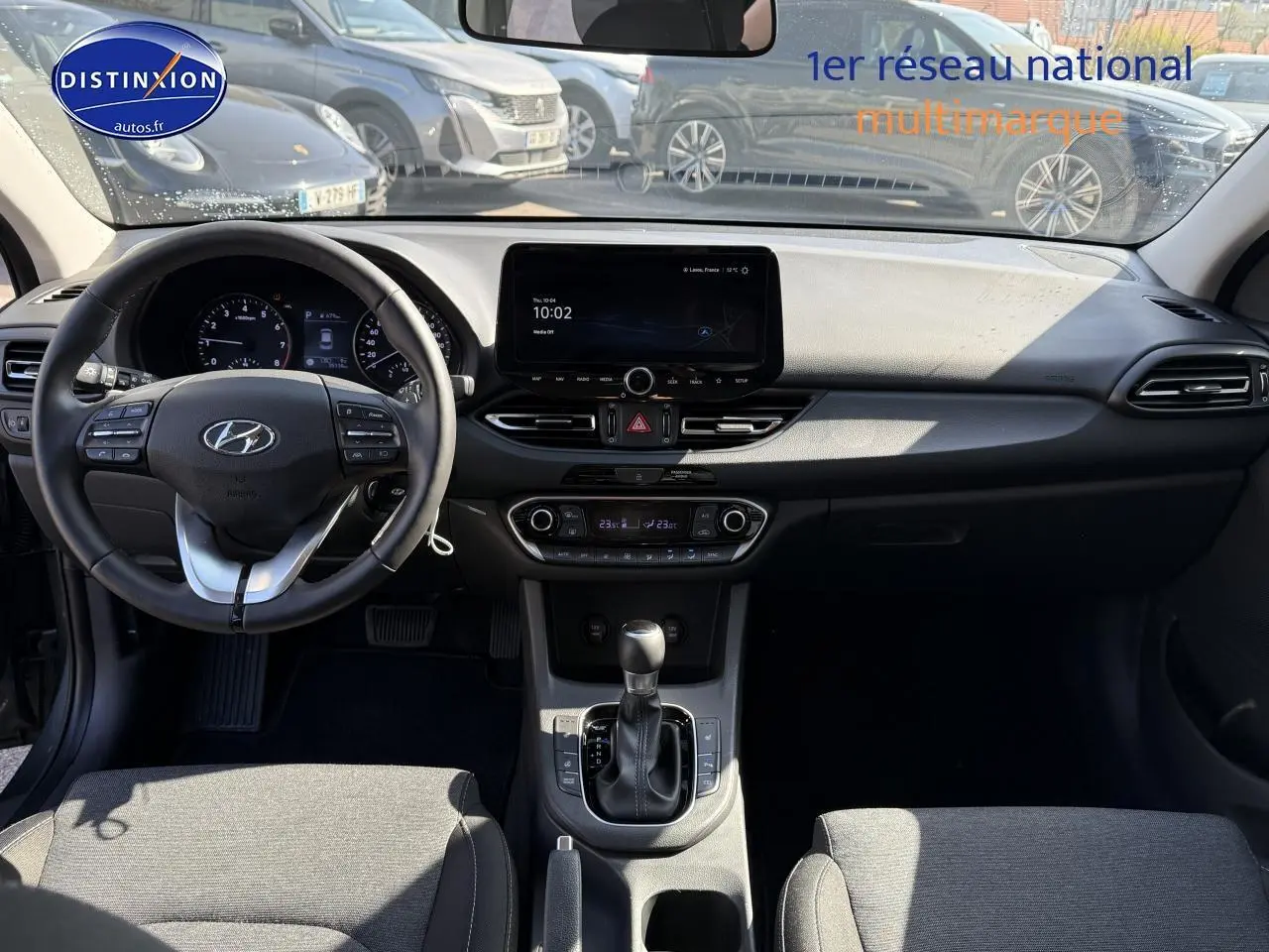 Intérieur de la Hyundai i30 2024 vue de face, tableau de bord noir avec écran tactile et volant multifonction cuir.