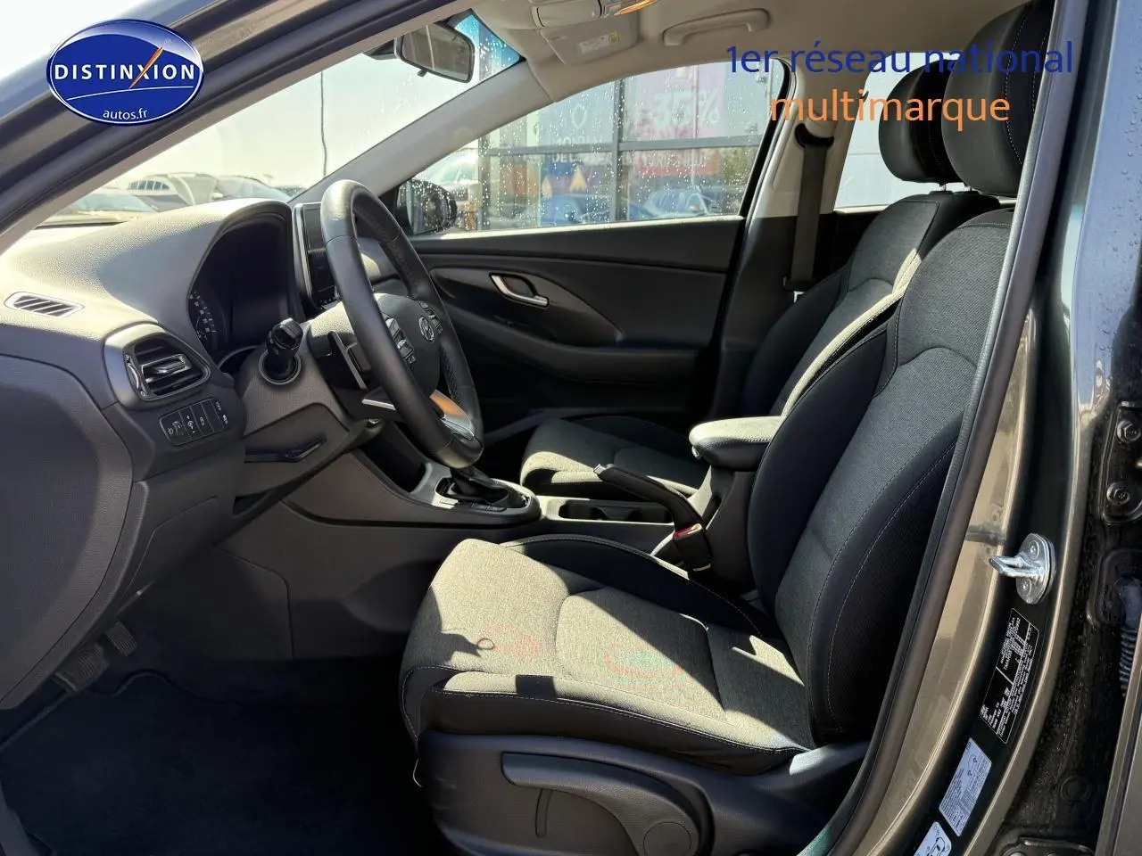 Intérieur avant droit de la Hyundai i30 2024 gris anthracite, sièges tissu et volant cuir multifonction visible.