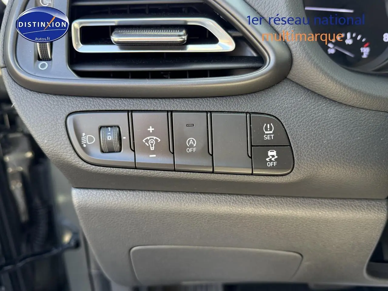 Vue rapprochée des commandes de réglage d'éclairage et d'assistance sur le tableau de bord gris foncé d'une Hyundai i30 2024.