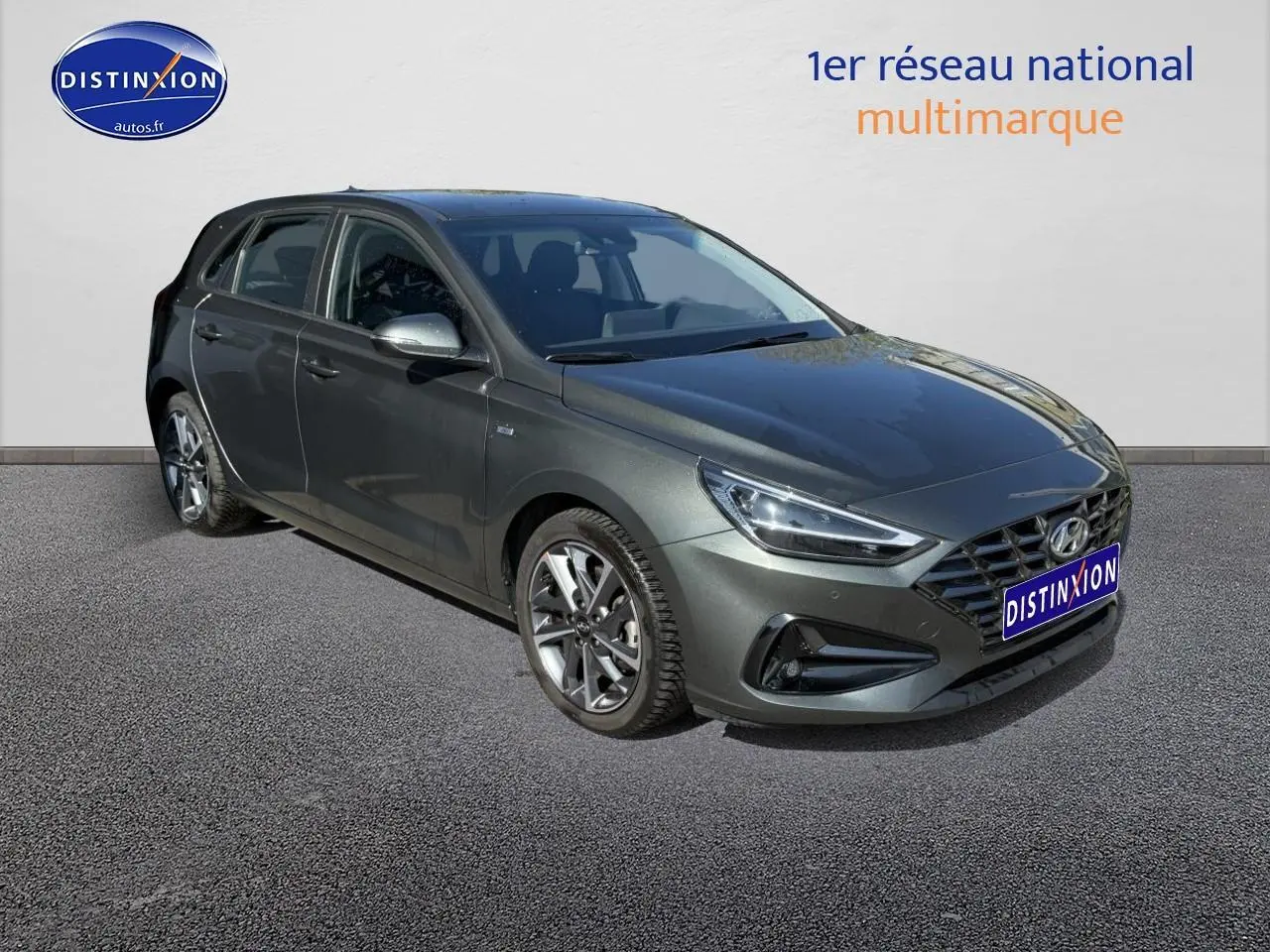 Hyundai i30 gris anthracite vue 3/4 avant droit avec jantes alliage et calandre hexagonale distinctive.