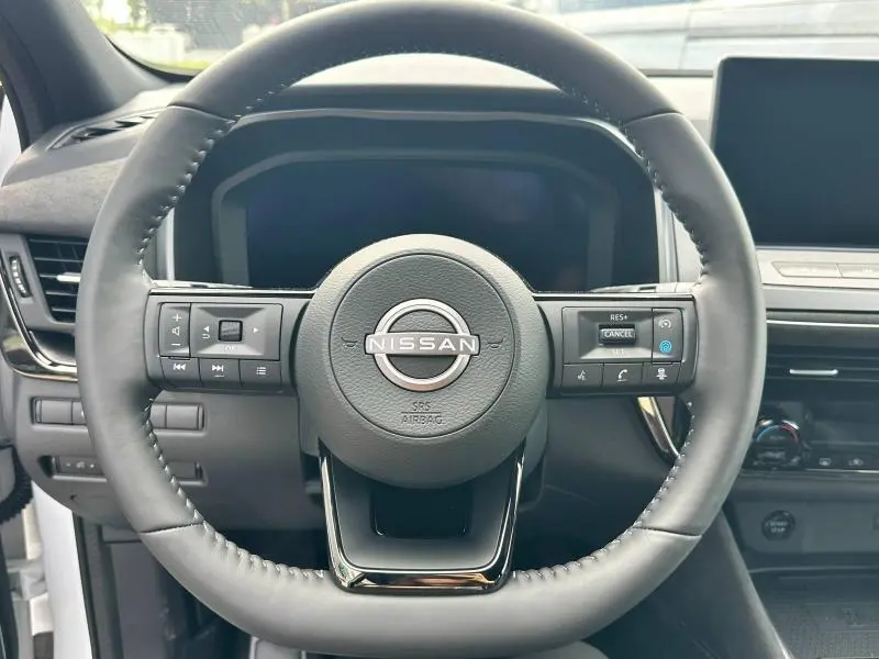 Volant en cuir noir du Nissan Qashqai e-POWER 2025, avec commandes intégrées et tableau de bord numérique en arrière-plan.