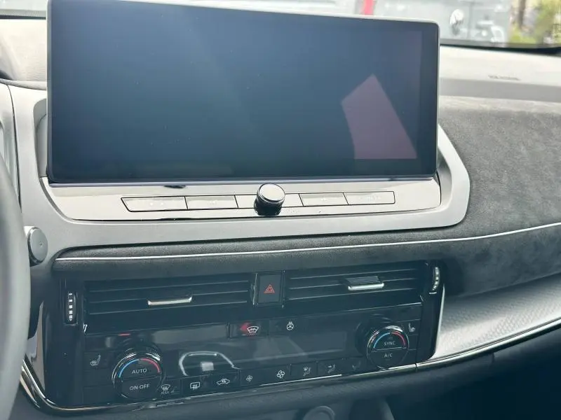 Tableau de bord du Nissan Qashqai e-POWER 2025 avec écran tactile large et commandes climatisation en vue frontale rapprochée.