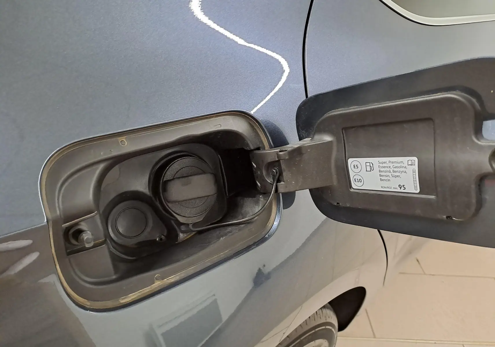 Gros plan sur la trappe à carburant ouverte côté gauche d’une SEAT LEON gris magnétique 2025, détail essence.