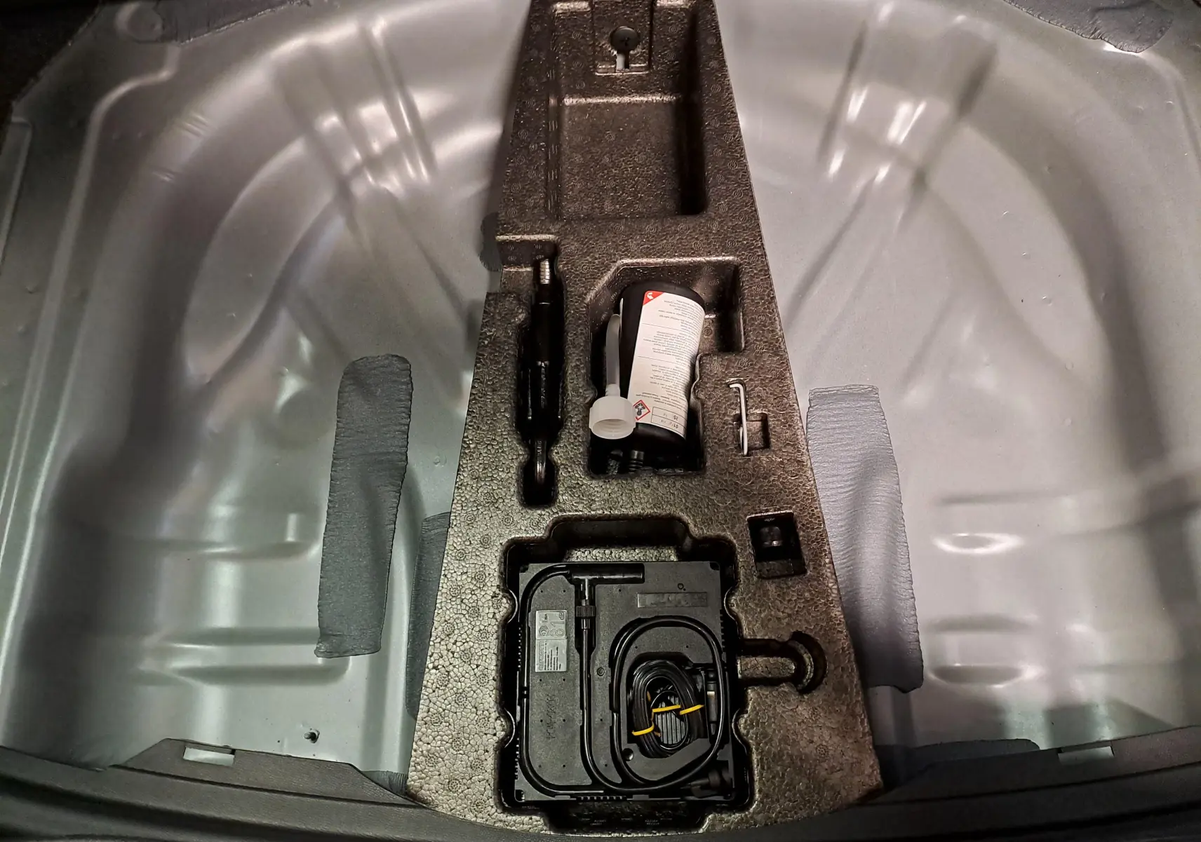 Vue plongeante sur le coffre ouvert d'une SEAT LEON gris magnétique, montrant le rangement d'outils et compresseur intégré.