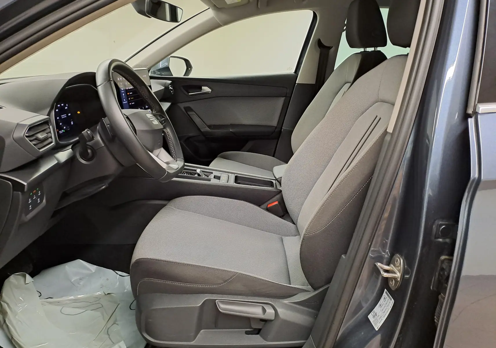Intérieur côté conducteur du SEAT Leon 2025 gris magnétique, montrant sièges tissu gris et tableau de bord moderne.