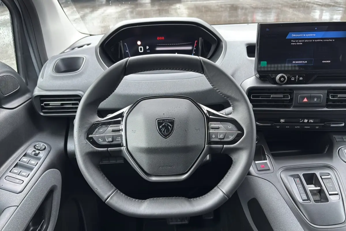 Vue centrée sur le volant cuir multifonctions et tableau de bord numérique du Peugeot Rifter 2026, intérieur gris.