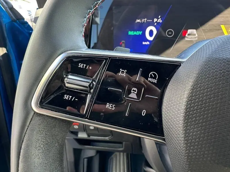 Gros plan sur les commandes du volant côté gauche du Renault Rafale bleu, avec affichage numérique en arrière-plan.