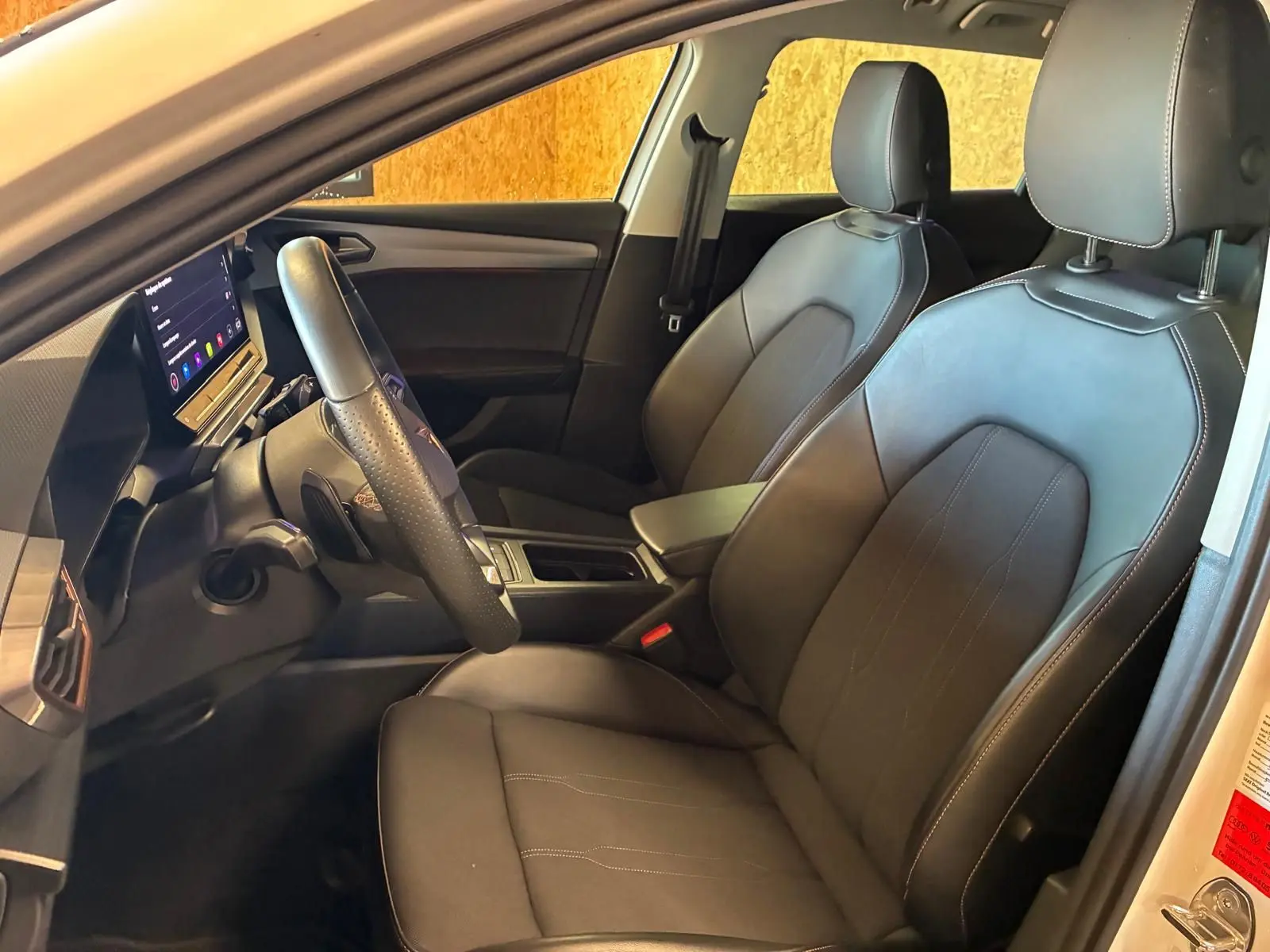 Vue intérieure côté conducteur de la CUPRA LEON ST 2024, sièges noirs en cuir avec surpiqûres contrastées.