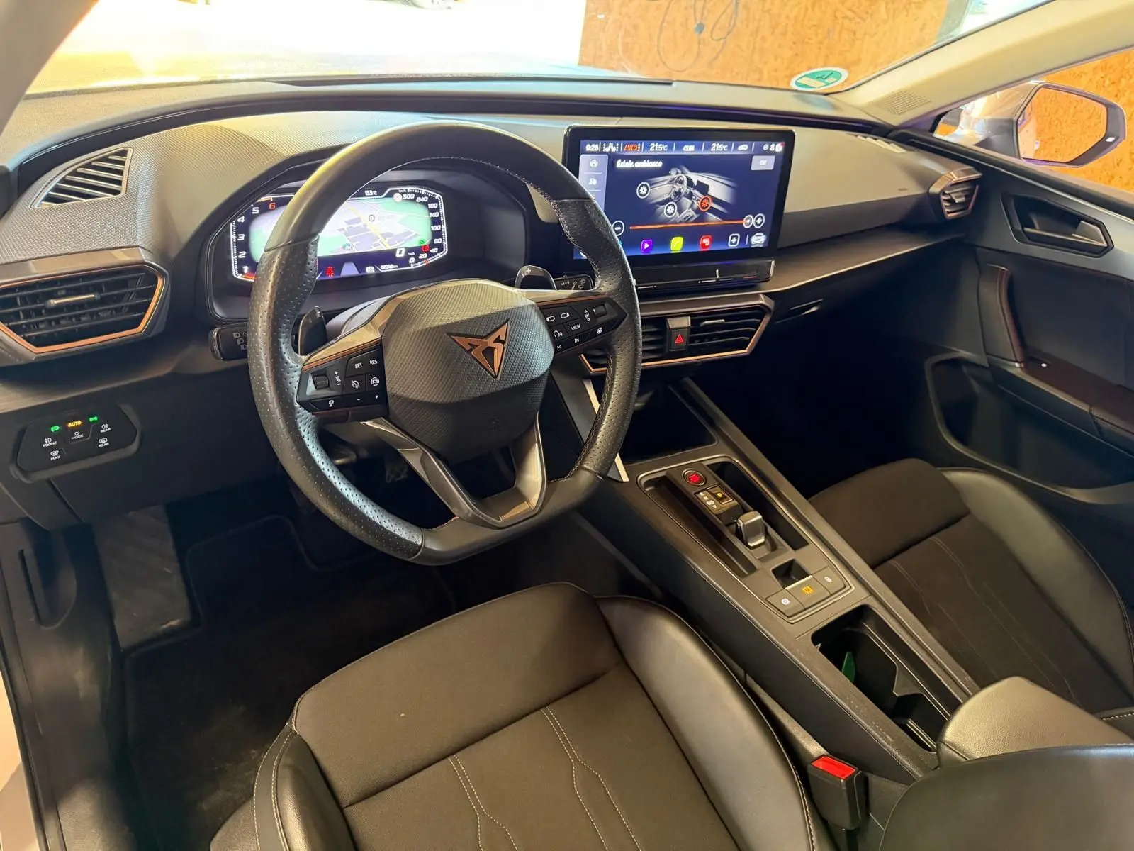 Poignée de porte intérieure côté gauche avec couture orange sur fond noir, partie d’une CUPRA LEON ST blanche 2024.