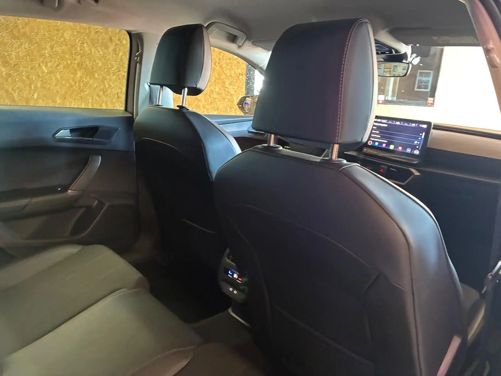 Vue intérieure arrière de la CUPRA Leon ST 2024 avec sièges en cuir noir et écran tactile central visible à l'avant.