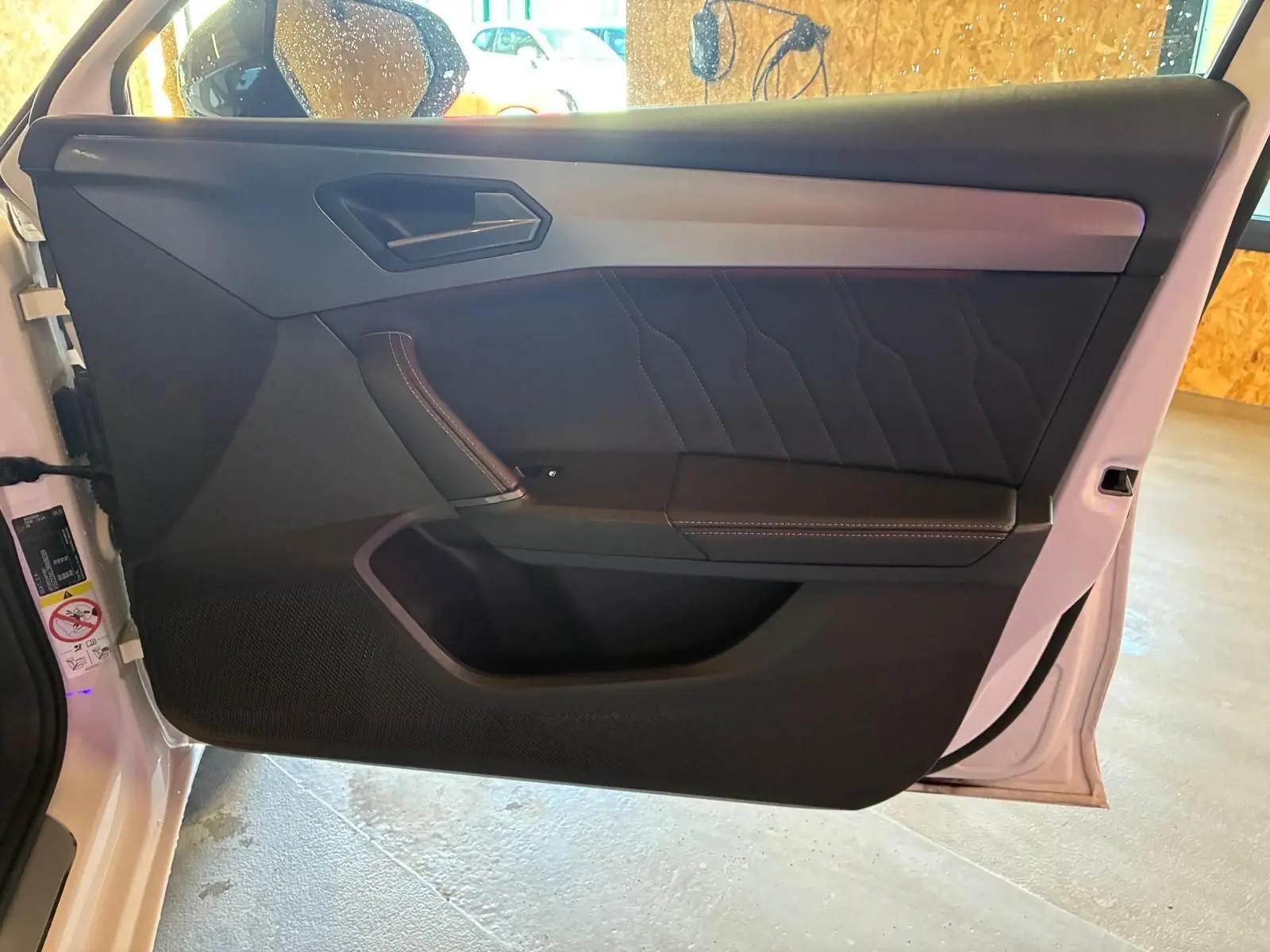 Vue intérieure de la porte avant gauche blanche d'une CUPRA LEON ST 2024 avec garniture noire et surpiqûres contrastées.