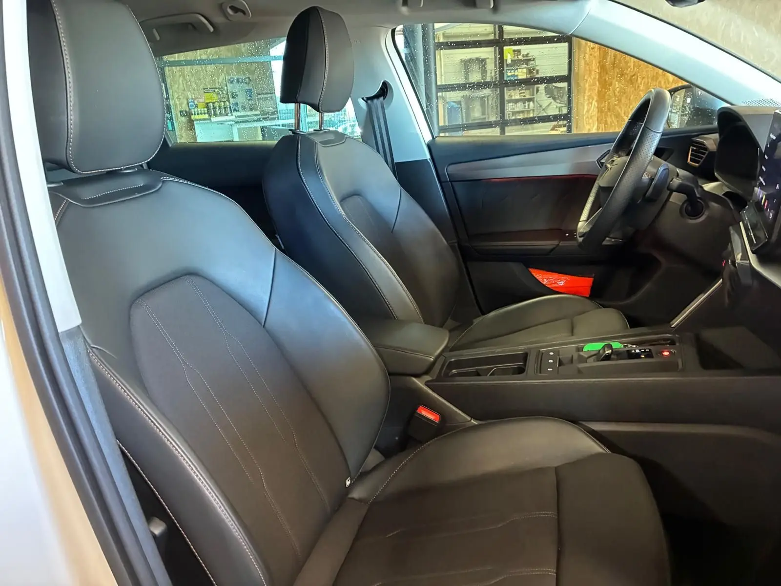Vue intérieure côté conducteur de la CUPRA LEON ST 2024, sièges noirs avec surpiqûres blanches et console centrale moderne.