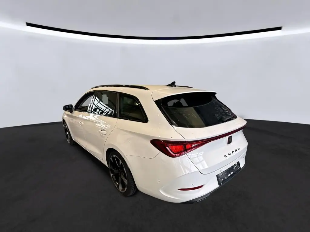 Vue 3/4 arrière droite d'une CUPRA Leon ST blanche 2024 avec toit noir et jantes noires dans un studio épuré.