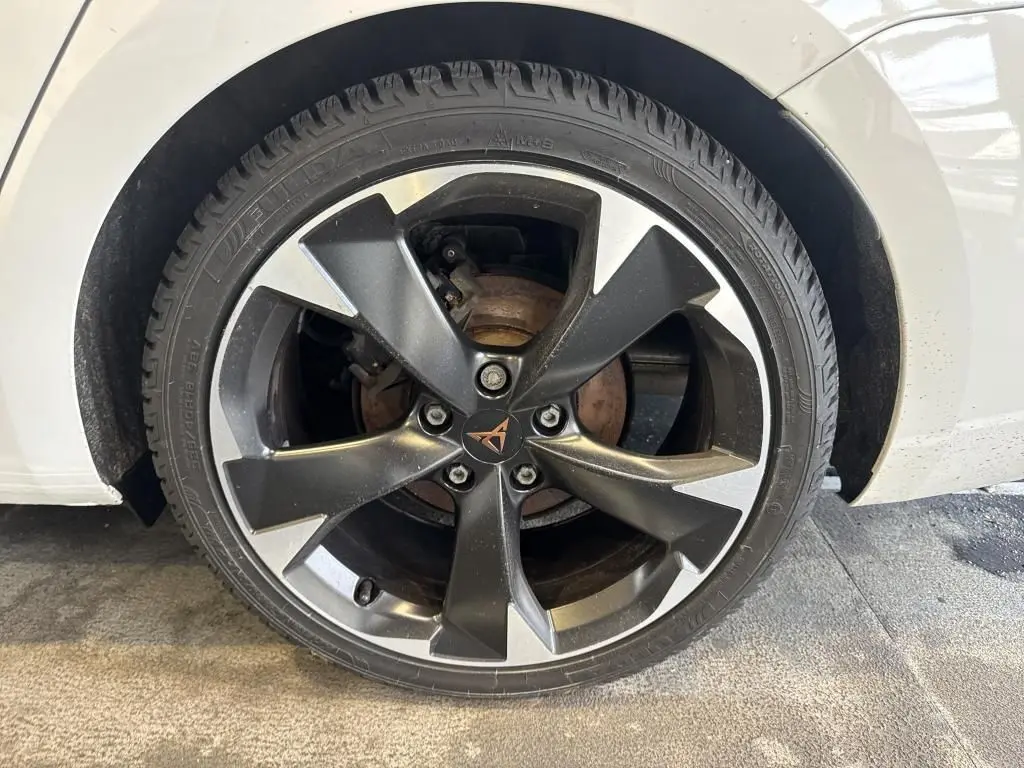 Gros plan sur la roue avant droite d'une CUPRA LEON ST blanche, mettant en valeur la jante alliage noire et argentée au logo CUPRA central.