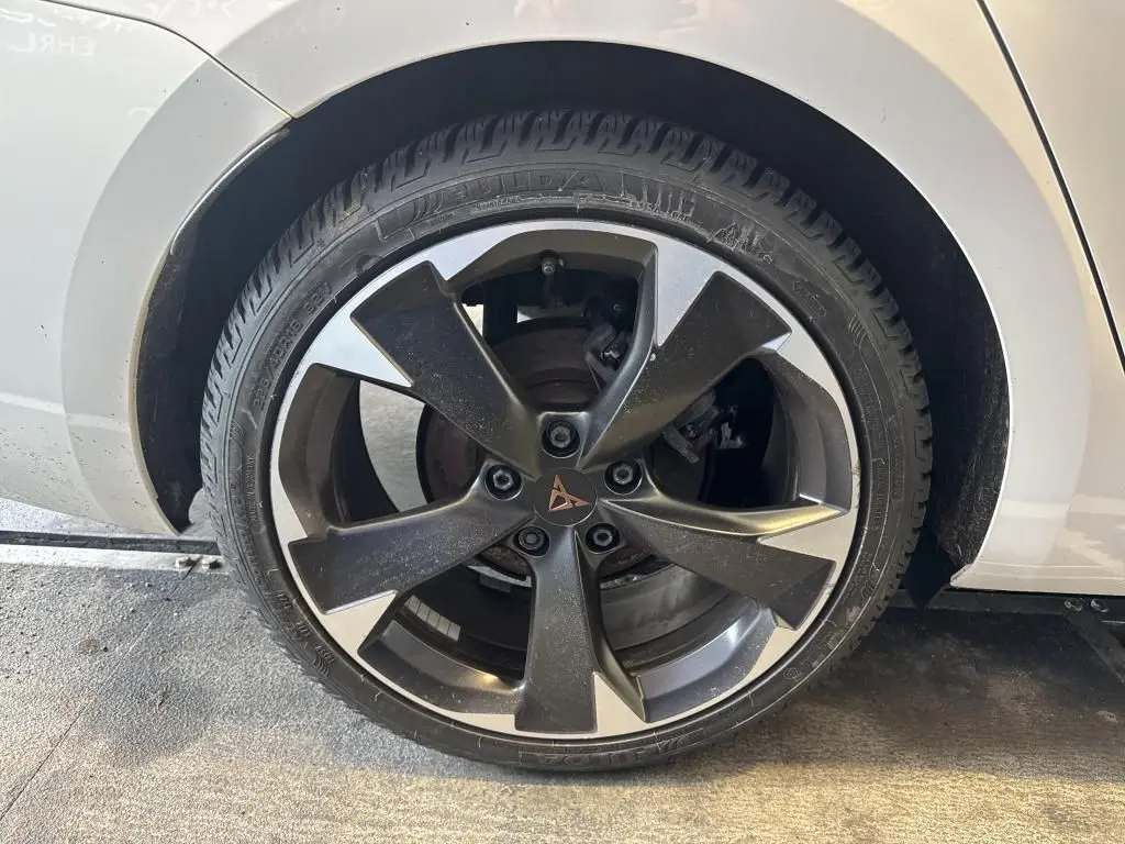 Gros plan sur la roue avant gauche d'une CUPRA LEON ST blanche, jante alliage noire et argentée au design moderne.