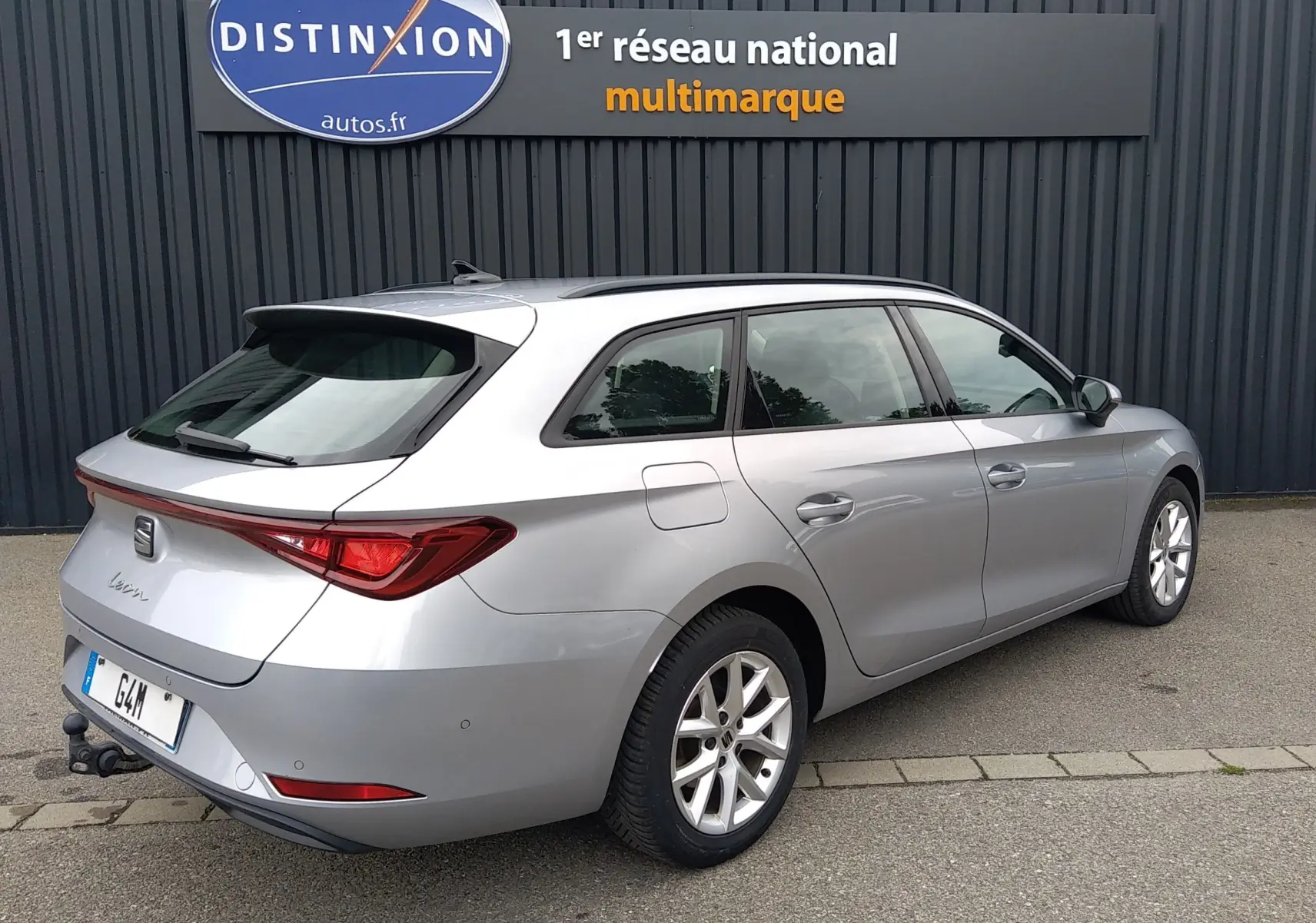 SEAT Leon ST gris vue 3/4 arrière droit, break hybride essence avec barres de toit et attelage visible.