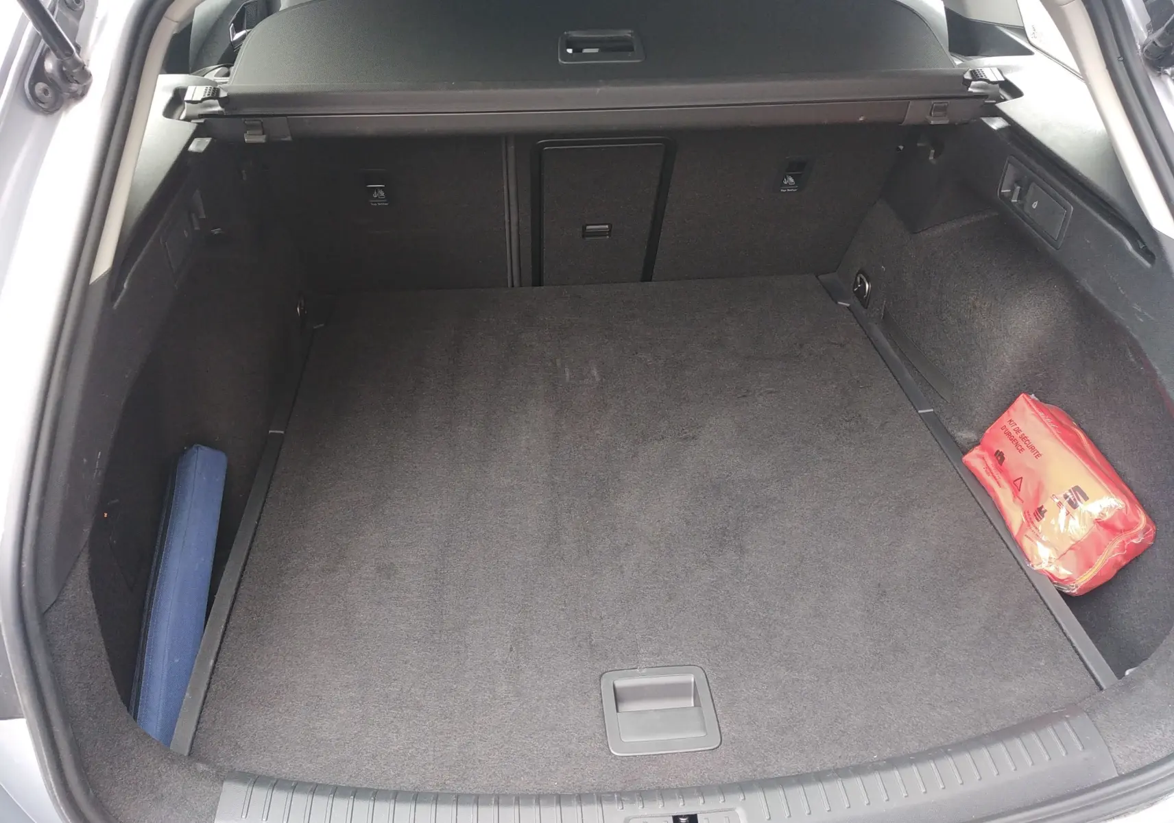 Coffre ouvert d'une SEAT LEON ST gris, vue de l'arrière montrant un espace de chargement propre avec trousse de secours rouge.