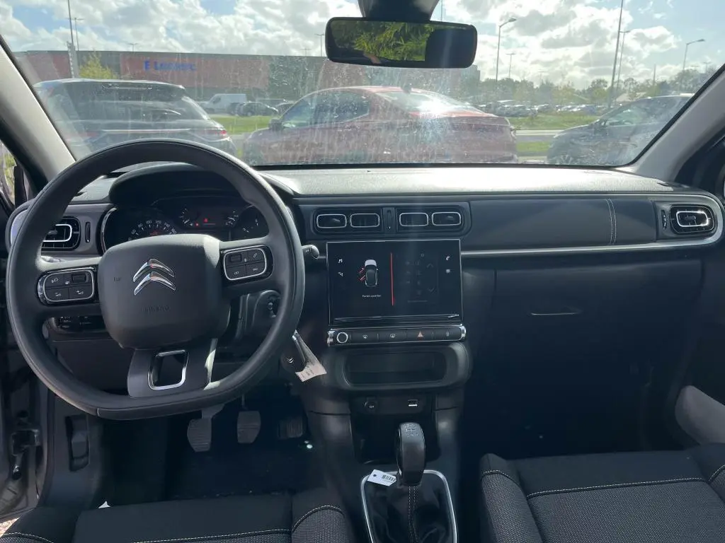 Vue intérieure avant du tableau de bord noir de la Citroën C3 gris 2022 avec volant multifonction et écran tactile central.