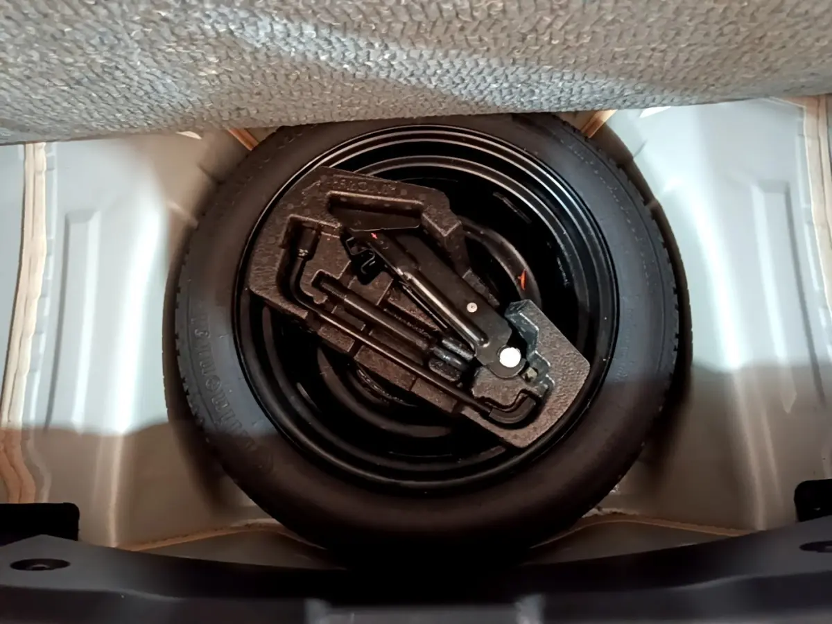 Gros plan sur la roue de secours et le kit d'outils dans le coffre d'une Citroën C1 gris clair.