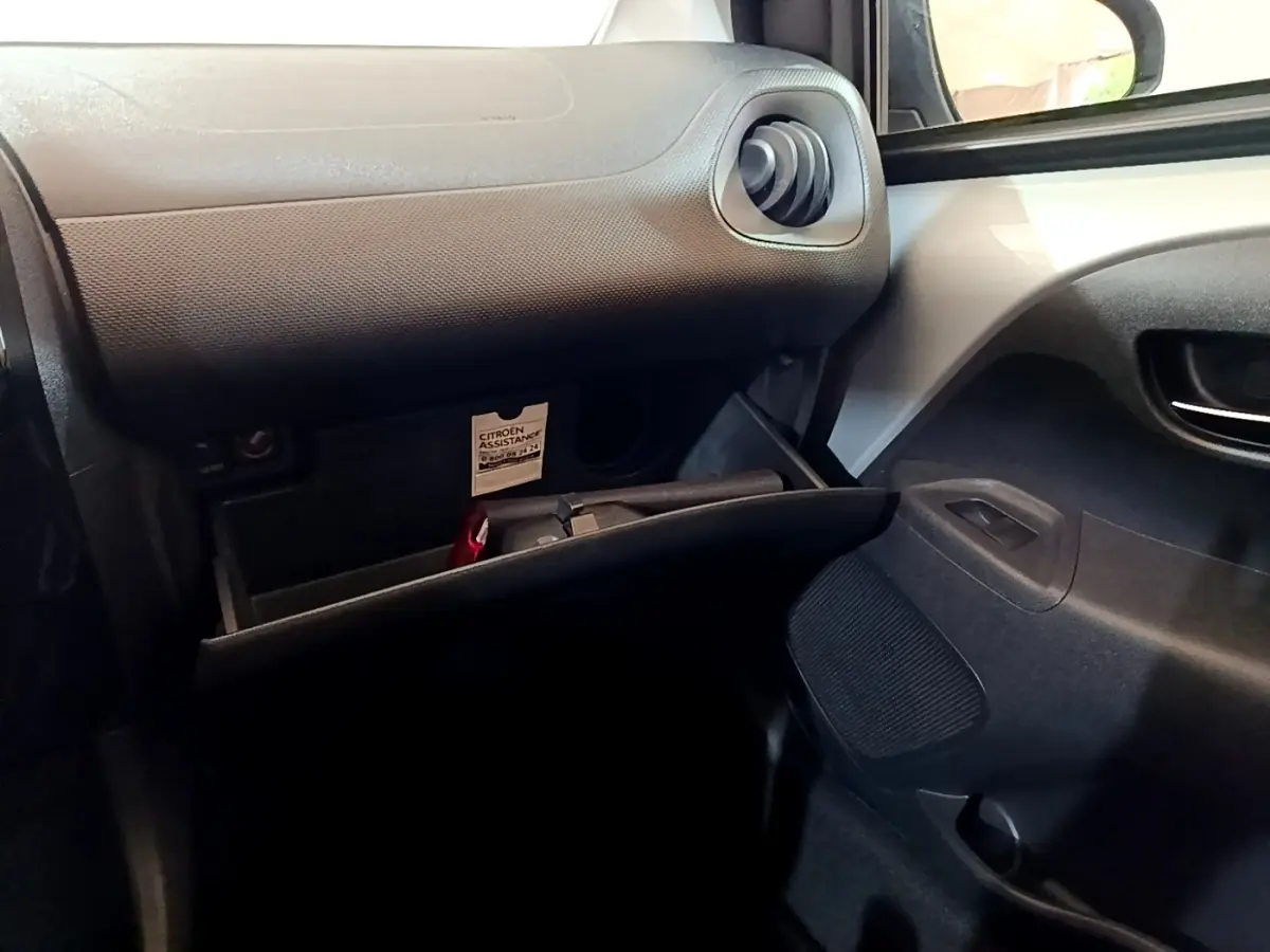 Intérieur côté passager d'une Citroën C1 gris clair 2019, boîte à gants ouverte avec ventilation ronde visible.