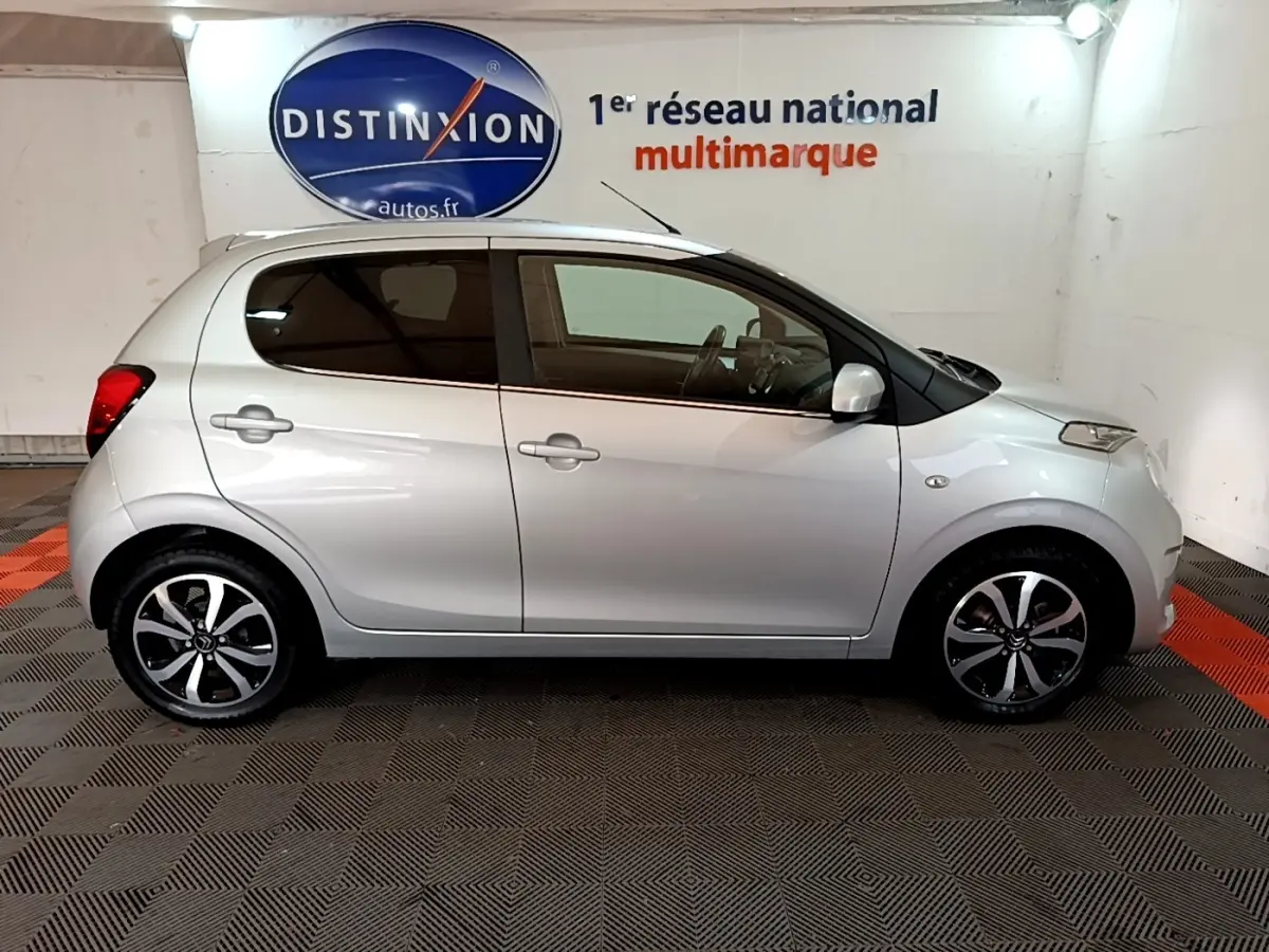 Profil droit d'une Citroën C1 gris clair 2019 avec jantes alliage noires et vitres teintées en intérieur showroom.