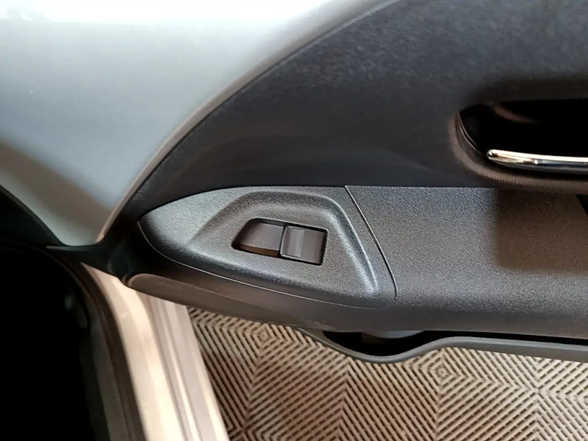 Gros plan sur la commande de réglage des rétroviseurs côté conducteur d’une Citroën C1 gris clair, intérieur noir.