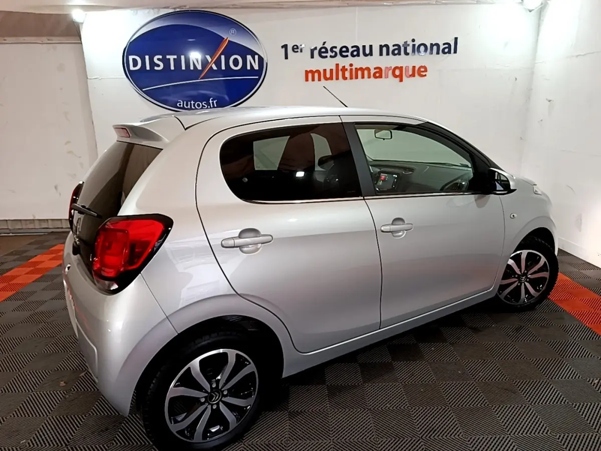 Citroën C1 gris clair vue de profil côté droit en intérieur avec jantes noires et rouges arrière visibles.
