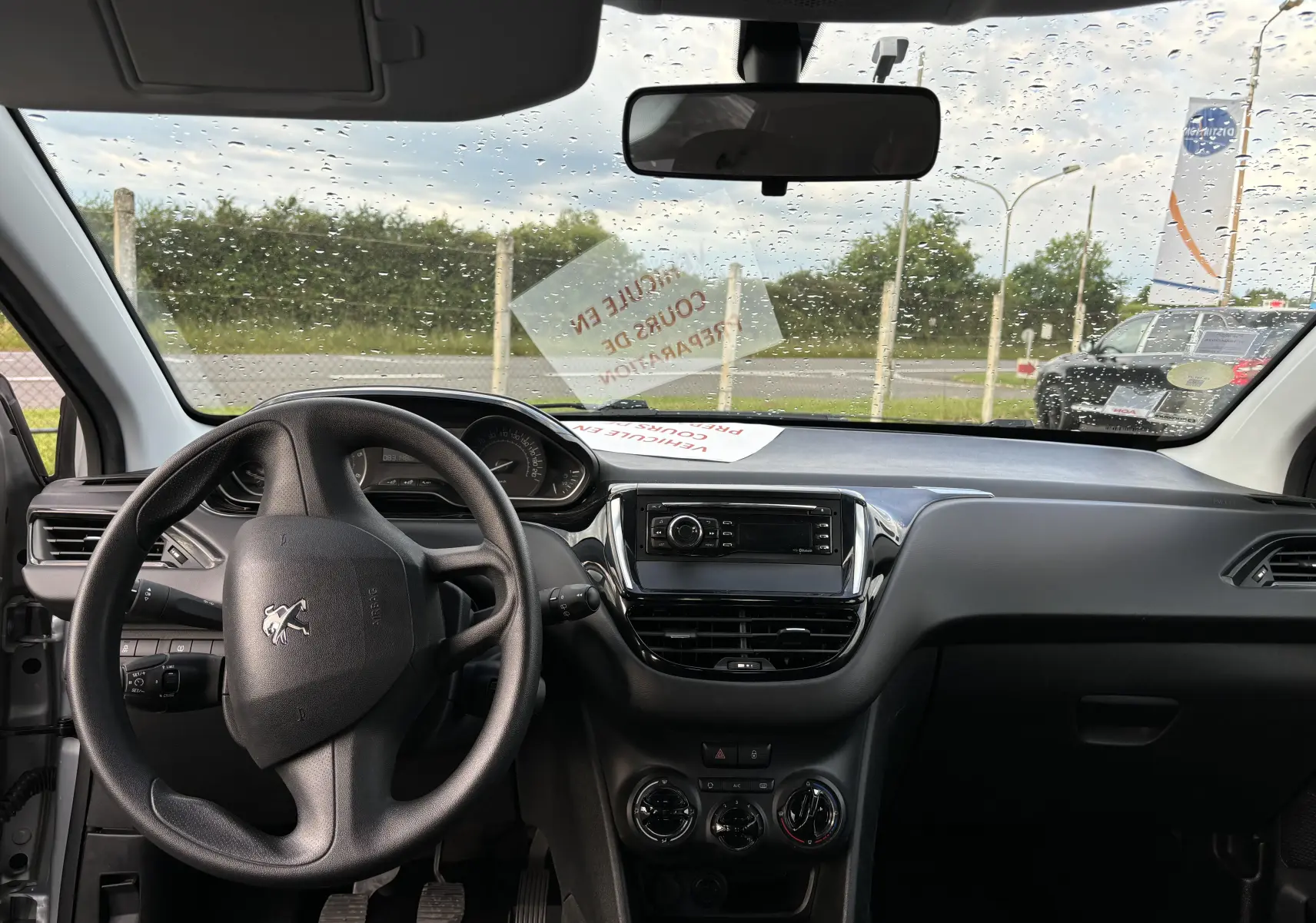 Vue intérieure avant du tableau de bord noir de la Peugeot 208 gris argent 2017 avec volant et système audio central.