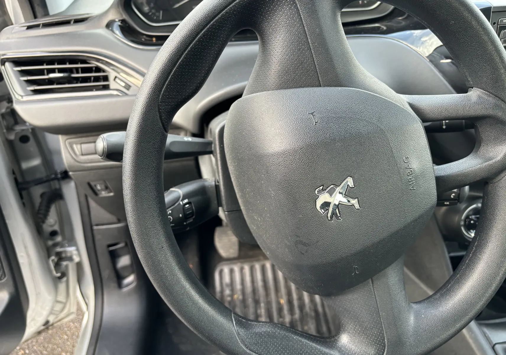 Vue rapprochée du volant noir de la Peugeot 208 gris argent 2017, avec tableau de bord et portière côté gauche visibles.