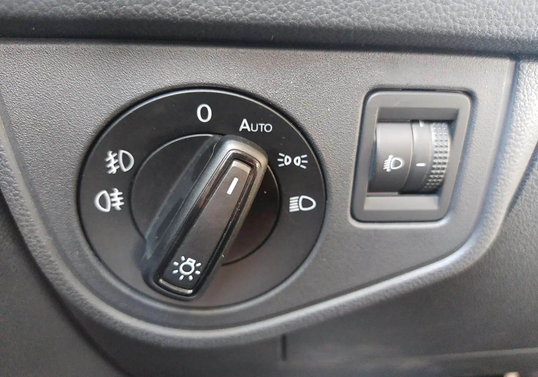 Gros plan sur le sélecteur de phares noir et la molette de réglage d'intensité lumineuse dans une Volkswagen Polo blanche 2021.