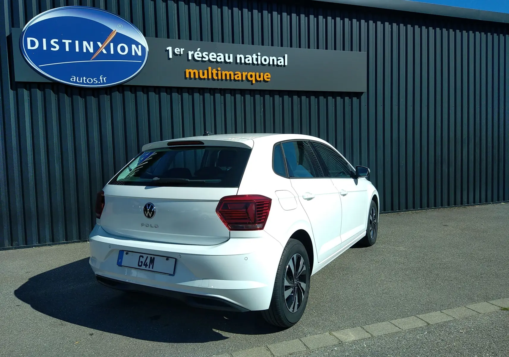 Vue 3/4 arrière droite d'une Volkswagen Polo blanche 5 portes garée devant un mur gris avec enseigne Distinxion.